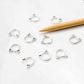 Eight silver cat-face ring stitch markers scattered on white background with bamboo knitting needle