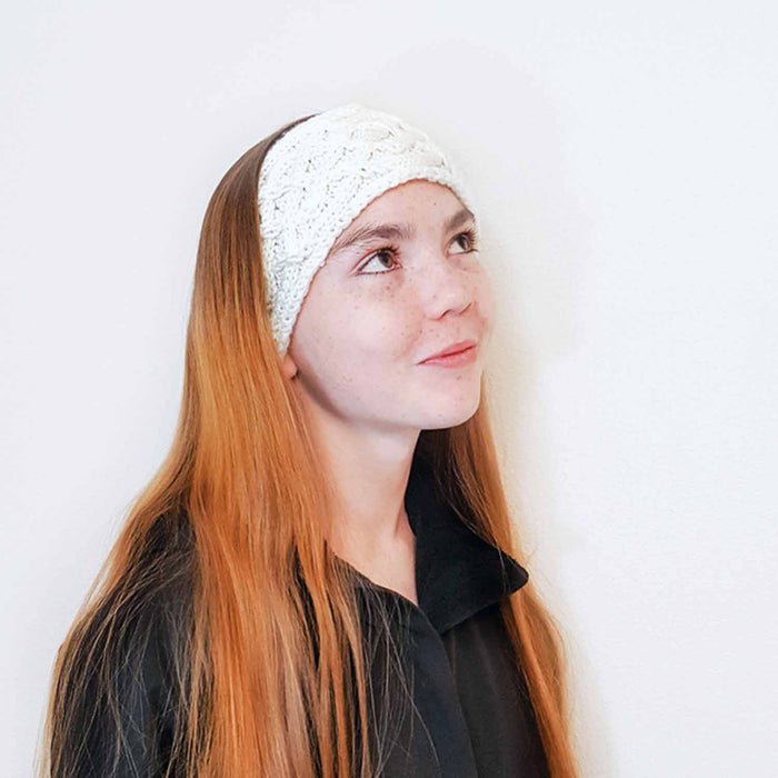 Girl wearing cream cable-knit Sorcha headband looking upward with long red hair