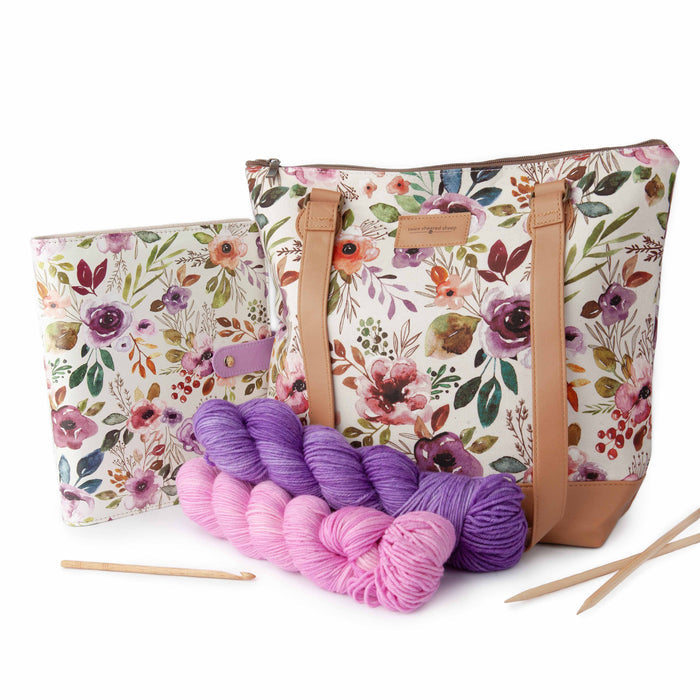 Spring Floral Mega Trinity Bag next to a matching smaller Trinity Bag with pink and purple yarn skeins, bamboo needles, and a crochet hook in front