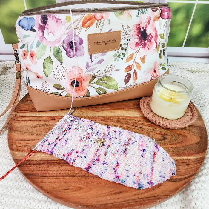 Spring Floral Trinity Bag styled on a wooden tray with a knitting project in progress, row counter chain, and a candle nearby