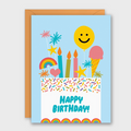 A colorful birthday card with a light blue border and an orange envelope behind it. The card features a white lower section with the words “HAPPY BIRTHDAY!” in blue, decorated with illustrated candles, balloons, fireworks, a rainbow, stars, and sprinkles.