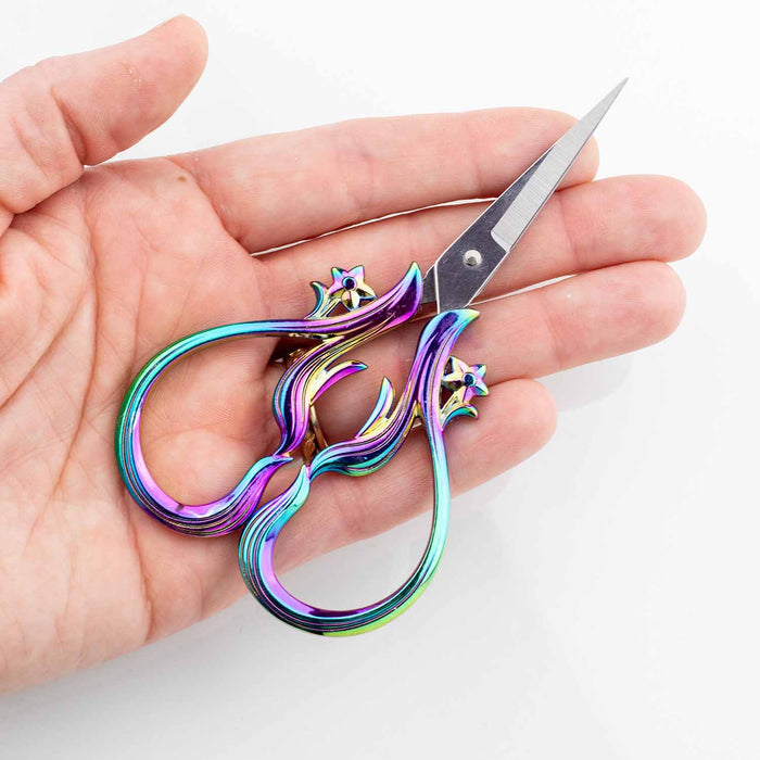 Hand holding the Star Dust Rainbow embroidery scissors showing the compact palm size with iridescent rainbow flame handles