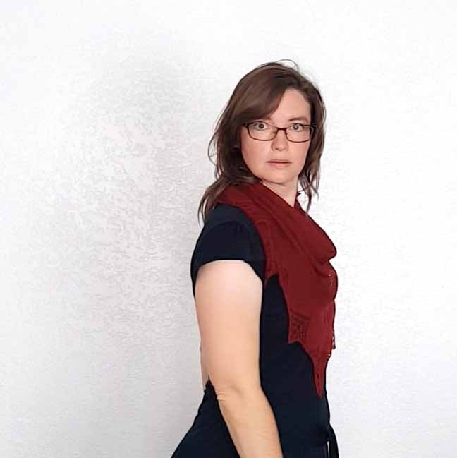 Woman wearing deep red Stardust lace shawl tied at the front over black dress with star point lace edging