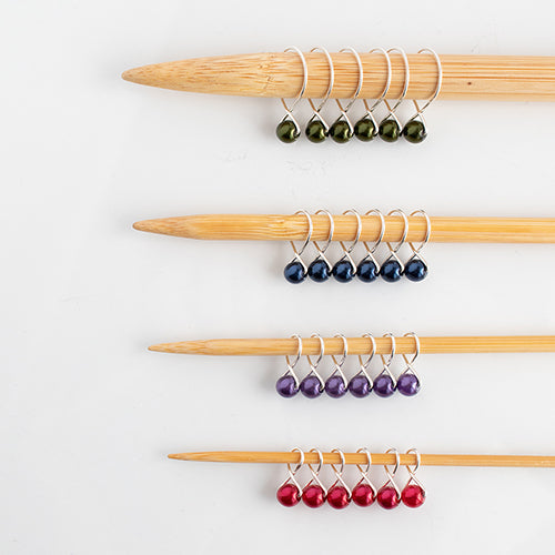 Fairy Lights stitch marker starter set with four rows of pearl bead markers in green, blue, purple, and red on bamboo knitting needles