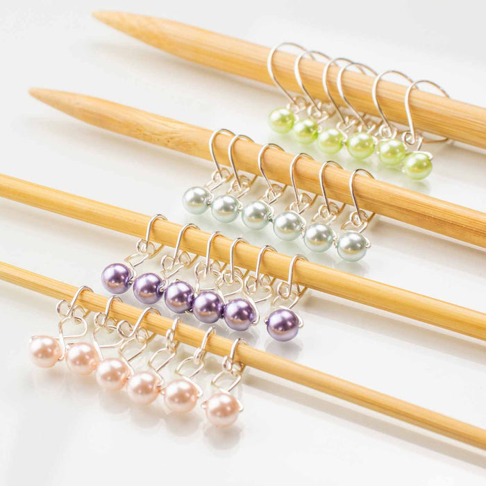 Four sets of melody clip style pastel pearl stitch markers in green, silver, purple, and pink on bamboo knitting needles