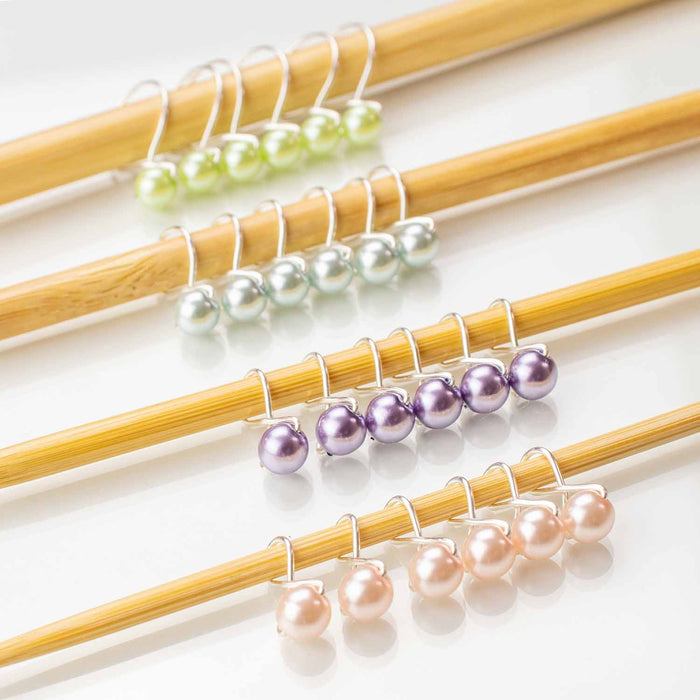 Four sets of infinity ring style pastel pearl stitch markers in green, silver, purple, and pink on bamboo knitting needles