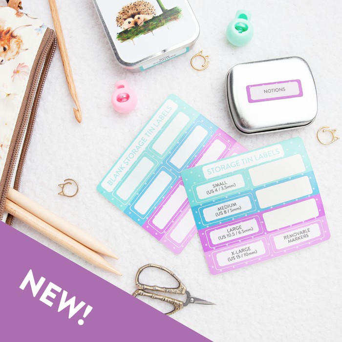 Storage tin label sticker sheets styled with knitting accessories including hedgehog storage tin, notions tin with purple label applied, cat stitch markers, wooden needles, and floral project bag