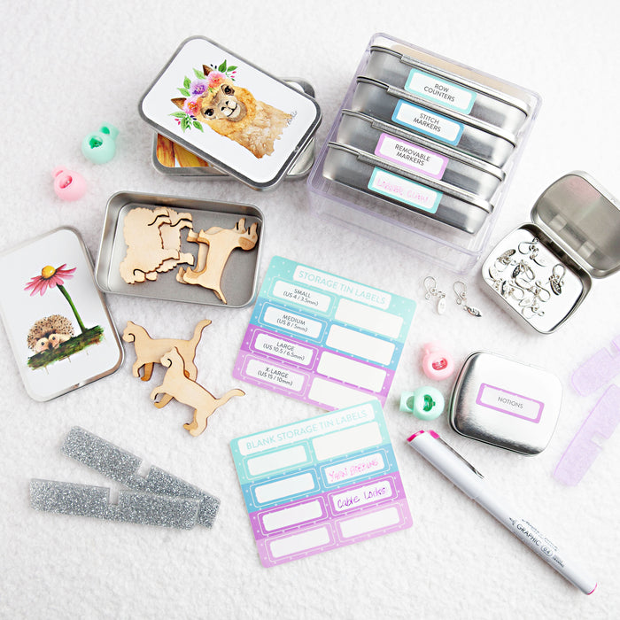 Full display of storage tin organization system showing labeled tins stacked in clear case, hedgehog and alpaca decorated tins, wooden animal figures, sticker label sheets, notions tin, and marker pen