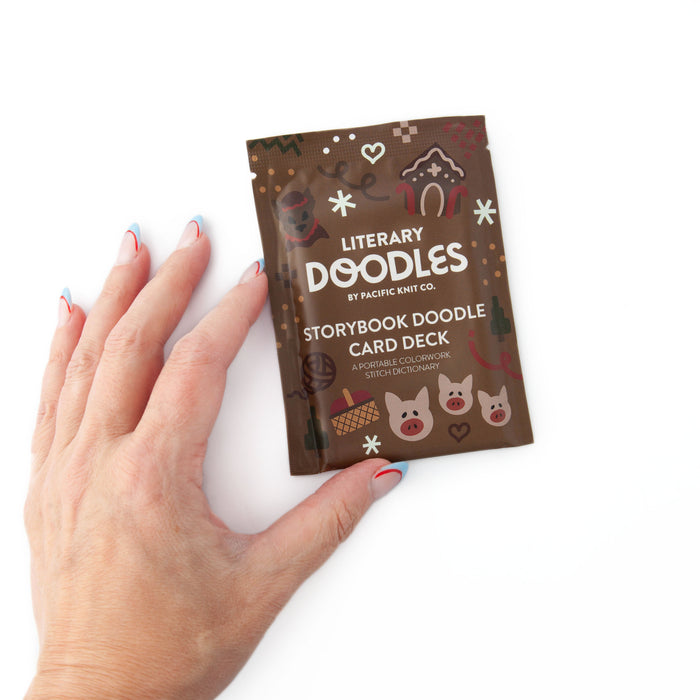 Hand resting beside the brown Literary Doodles Storybook Doodle Card Deck pouch on a white background, showing its size relative to a palm