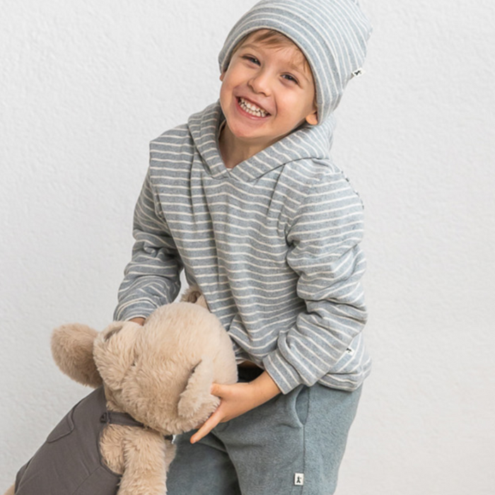 Child wearing a gray striped hoodie and holding a teddy bear against a white background