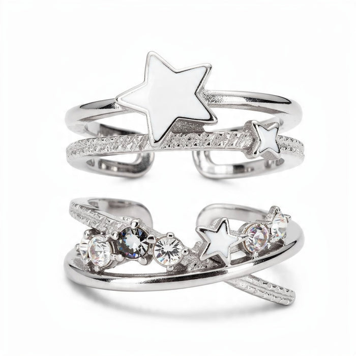 Silver celestial ring set on white background featuring white enamel stars, textured spiral bands, and clear crystal stones, stackable open adjustable rings