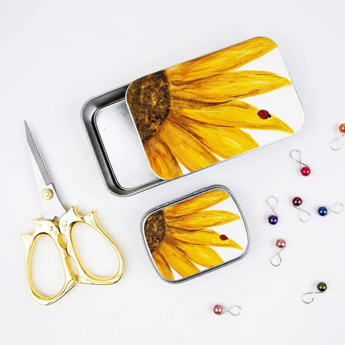 Both sunflower stitch marker tins styled with gold cat scissors and colorful stitch markers