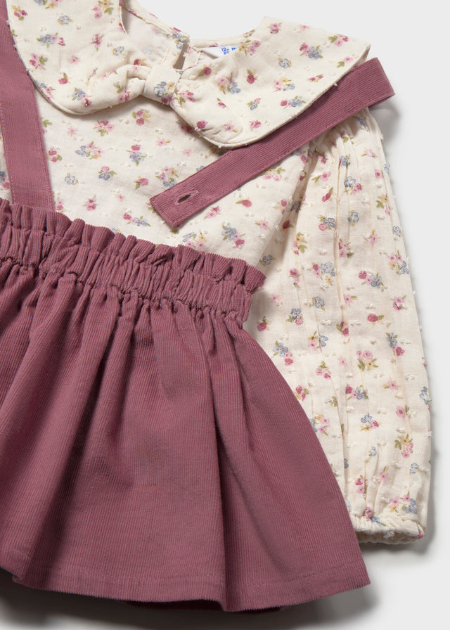 Children's outfit with floral top and purple skirt on a light gray background