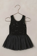 Black sequin dress on a hanger against a beige background