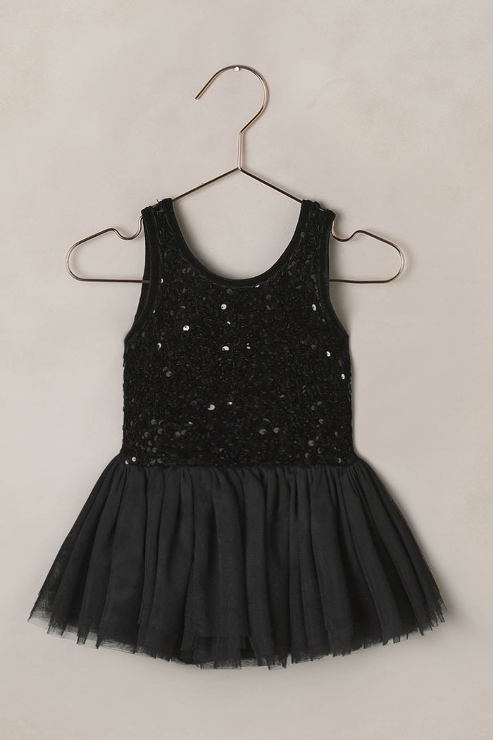 Black sequin dress on a hanger against a beige background