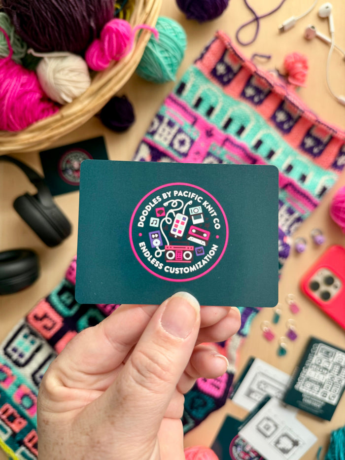 Hand holding the teal Pacific Knit Co card back with the Doodles logo