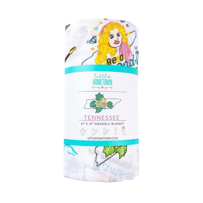 Fabric with colorful guitars, cars, barns, mountains, and text on a white background wrapped into packaging with ">Little Hometown" logo.
