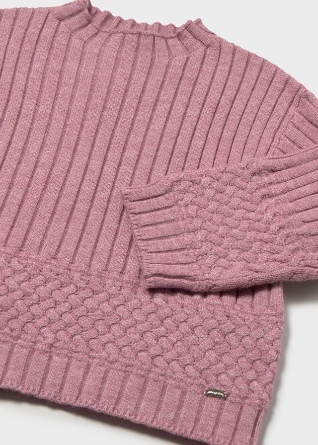Close-up of a ribbed knit sweater with a brand label on a light background