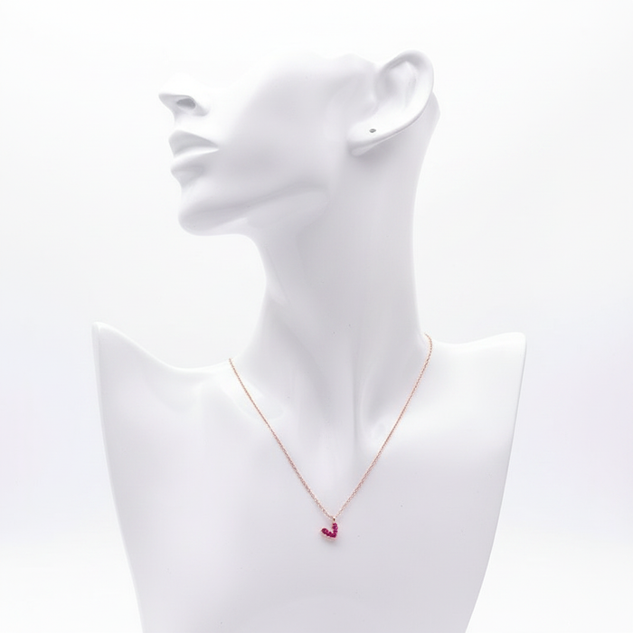 A high-resolution product shot of a dainty rose gold necklace featuring a small heart-shaped pendant pave-set with vibrant pink crystals, displayed on a sleek white bust mannequin against a pure white background.