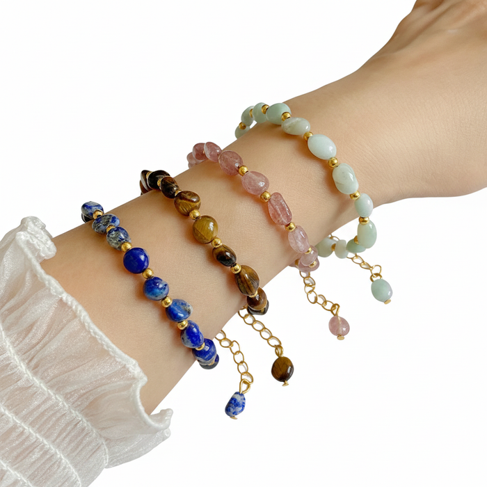 Four beaded gemstone bracelets in Lapis Lazuli, Tiger's Eye, Rose Quartz, and Amazonite with gold-tone accents and adjustable chains.
