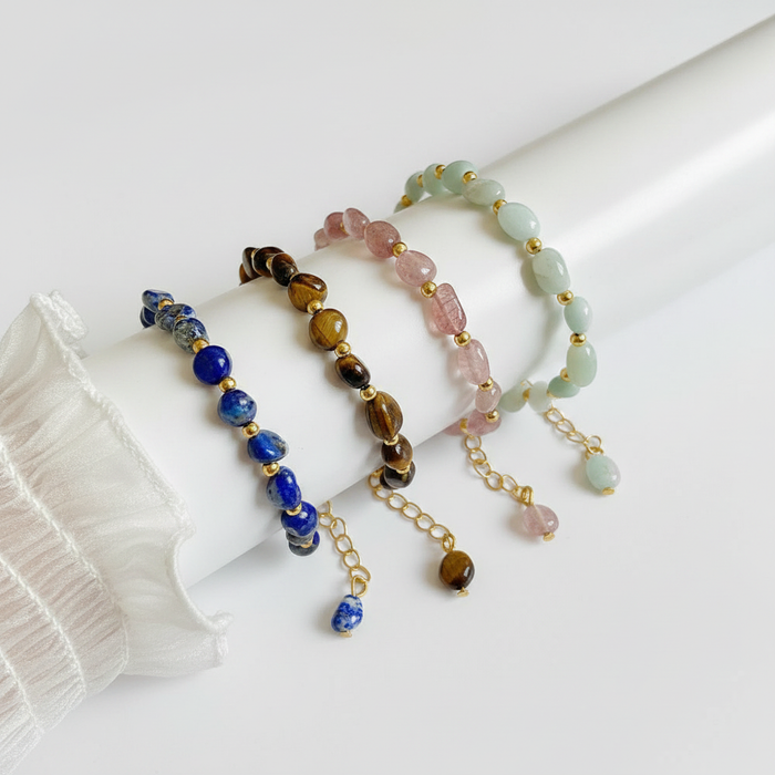 Four beaded gemstone bracelets in Lapis Lazuli, Tiger's Eye, Rose Quartz, and Amazonite with gold-tone accents and adjustable chains.