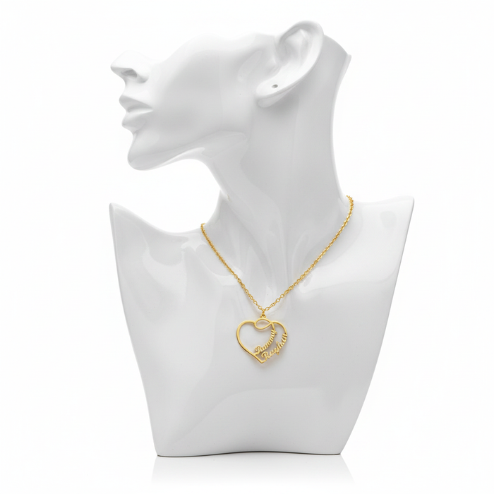 A high-resolution product shot of a personalized gold-plated necklace featuring a large open-heart pendant with two script names entwined within the design, displayed on a sleek white bust mannequin against a pure white background.