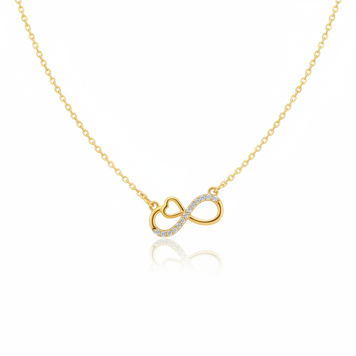 A gold-toned necklace featuring an infinity symbol pendant with an integrated heart detail. One side of the infinity loop is pavé-set with shimmering clear crystals. The pendant is attached to a fine gold cable chain and shown against a white background with a subtle reflection.