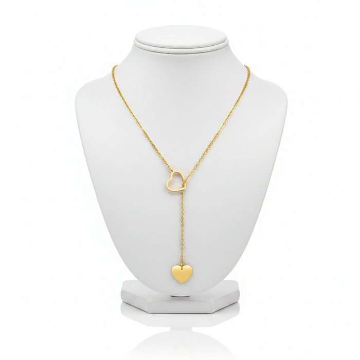 A high-resolution product shot of a gold heart lariat necklace featuring an open-heart slider and a solid heart pendant at the end of a drop chain, displayed on a classic white jewelry bust against a pure white background.