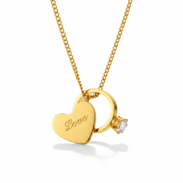 A gold-toned curb chain necklace featuring two distinct charms: a polished flat heart engraved with the word "Love" in script, and a miniature solitaire engagement-style ring with a clear, sparkling crystal set in a four-prong mount. The jewelry is presented on a crisp white background with a soft shadow.