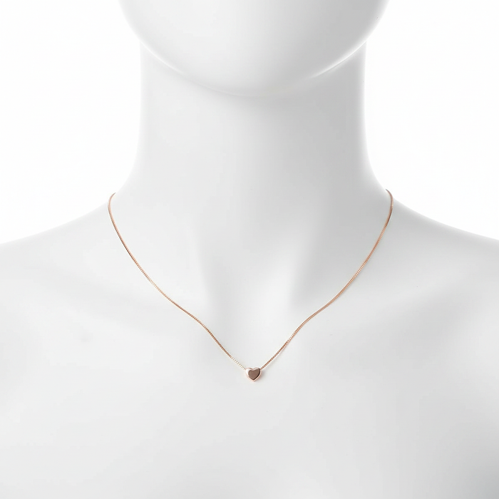 A close-up, high-resolution shot of a dainty rose gold necklace featuring a tiny, polished heart pendant on a thin box chain, displayed on a clean white jewelry mannequin against a pure white background.