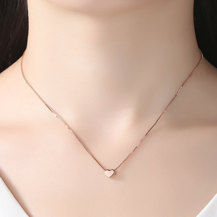 Rose gold dainty heart necklace on a thin box chain worn by a woman, minimalist romantic jewelry fashion.