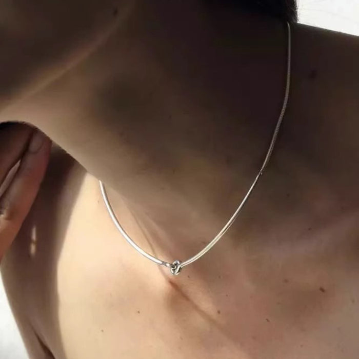 Minimalist silver snake chain necklace with a center knot detail worn on a woman's neck, geometric modern jewelry.