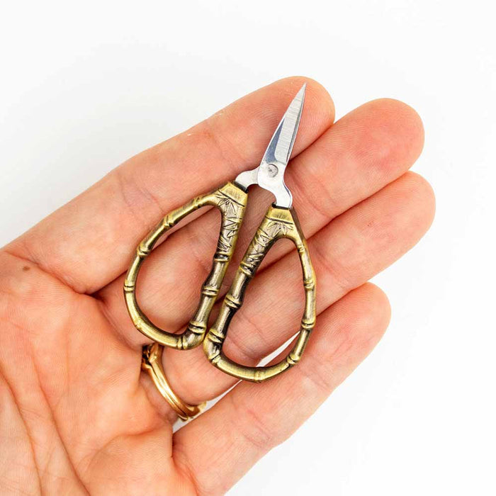 Hand holding bronze bamboo thread snips tiny scissors showing compact size against fingers