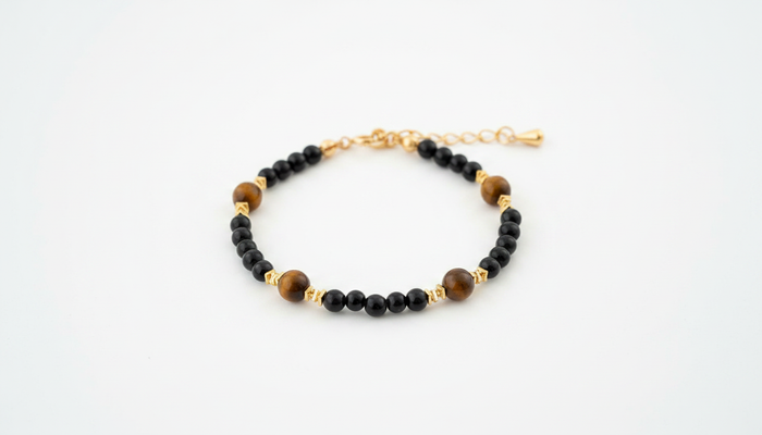 Beaded bracelet featuring polished black onyx beads and natural brown tiger’s eye stones with gold-tone spacers and an adjustable chain.