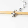 Close-up of silver sea turtle charm on numbered bead chain row counter resting on bamboo knitting needle