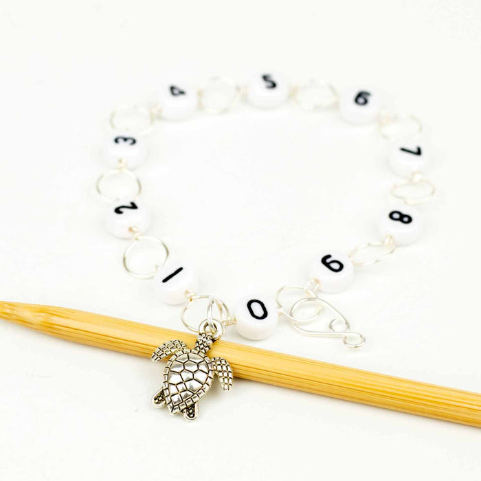 Sea turtle chain row counter in circle layout with numbered beads 0 through 9 and turtle charm on bamboo knitting needle