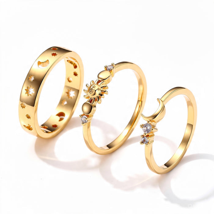 Three gold celestial rings on pure white background: wide band with moon and star cutouts, sun ring with crystal details, and open crescent moon ring with crystals