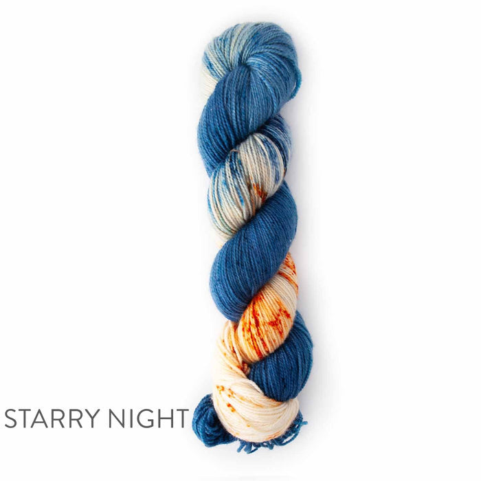 Single skein of TSS Classic Sock Paints yarn in Starry Night colorway featuring deep indigo blue sections with cream and orange speckled accents on a white background