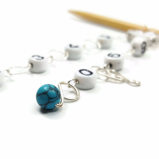 Close-up of turquoise gemstone bead on silver wire row counter chain with numbered beads on bamboo knitting needle