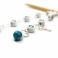 Close-up of turquoise gemstone bead on silver wire row counter chain with numbered beads on bamboo knitting needle