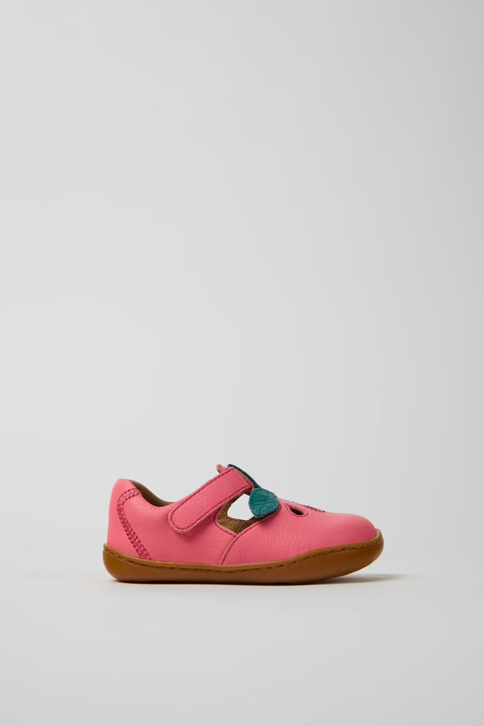Pink children's shoe with a brown sole on a light gray background