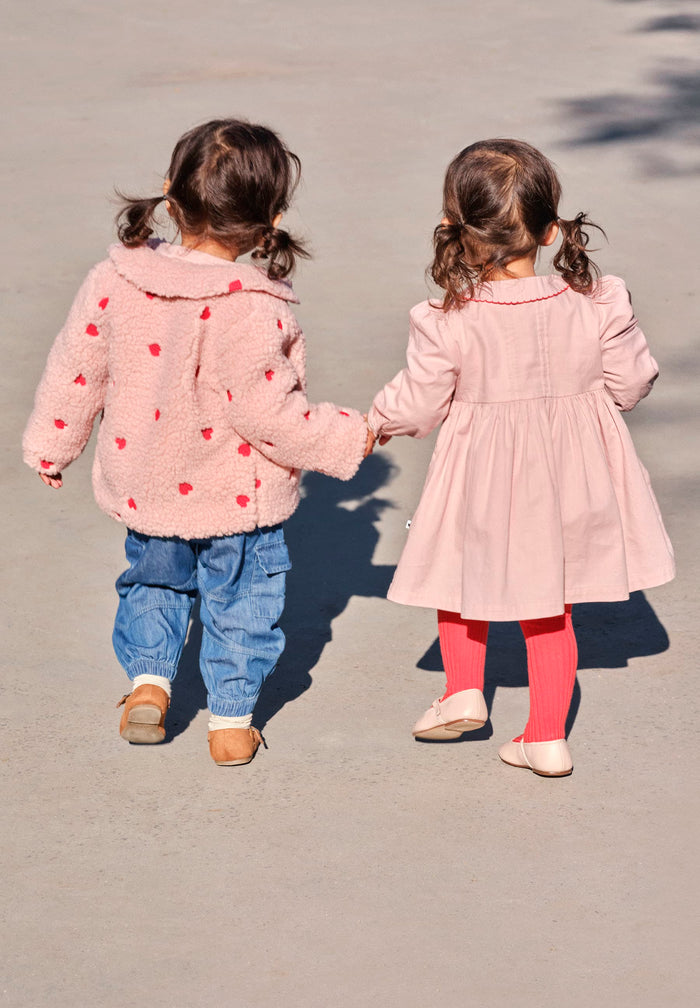 Two children in pink coats holding hands on a street.