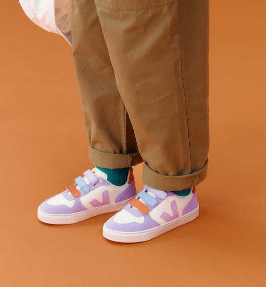 Person wearing pastel-colored sneakers with a plain orange background