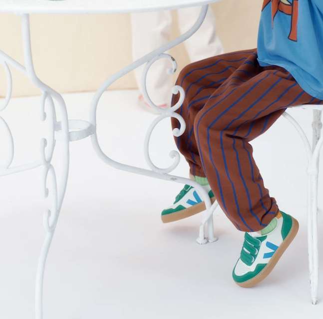Person wearing brown striped pants and green sneakers sitting on a white chair.