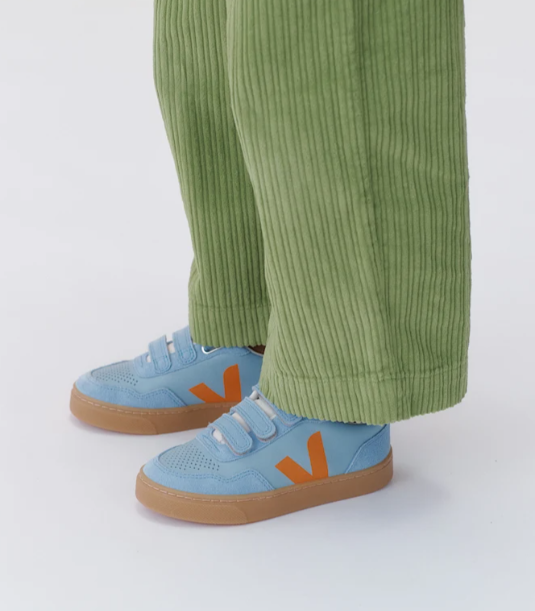 Blue sneakers with orange accents worn with green pants on a white background