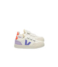 A pair of Veja Kids low-top sneakers in white leather, featuring a large purple 'V' logo on the side, double hook-and-loop straps, a purple heel tab, and a bright orange heel accent, set against a plain white background.