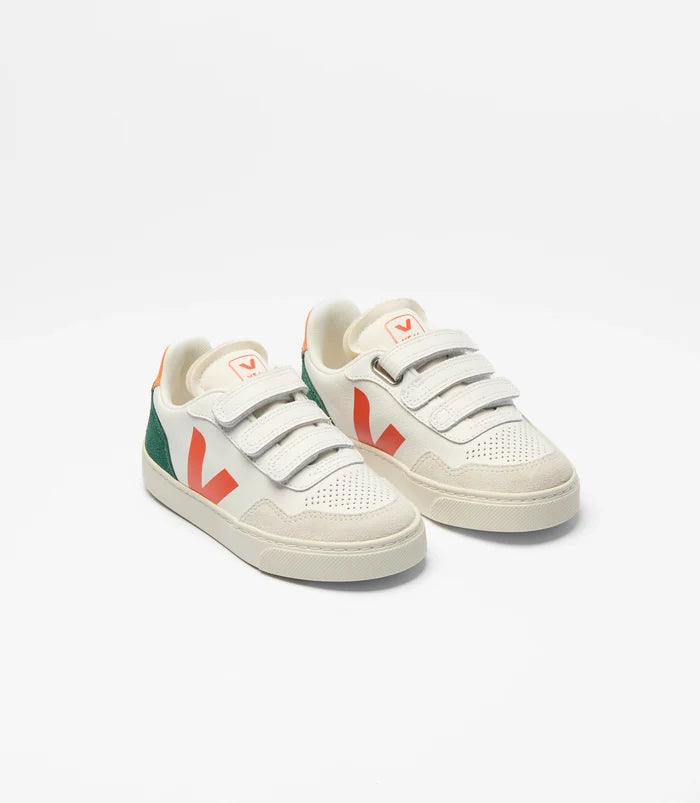 A pair of white low-top sneakers with three hook-and-loop straps, featuring orange and green logo accents on the sides and tongue, set against a plain white background.