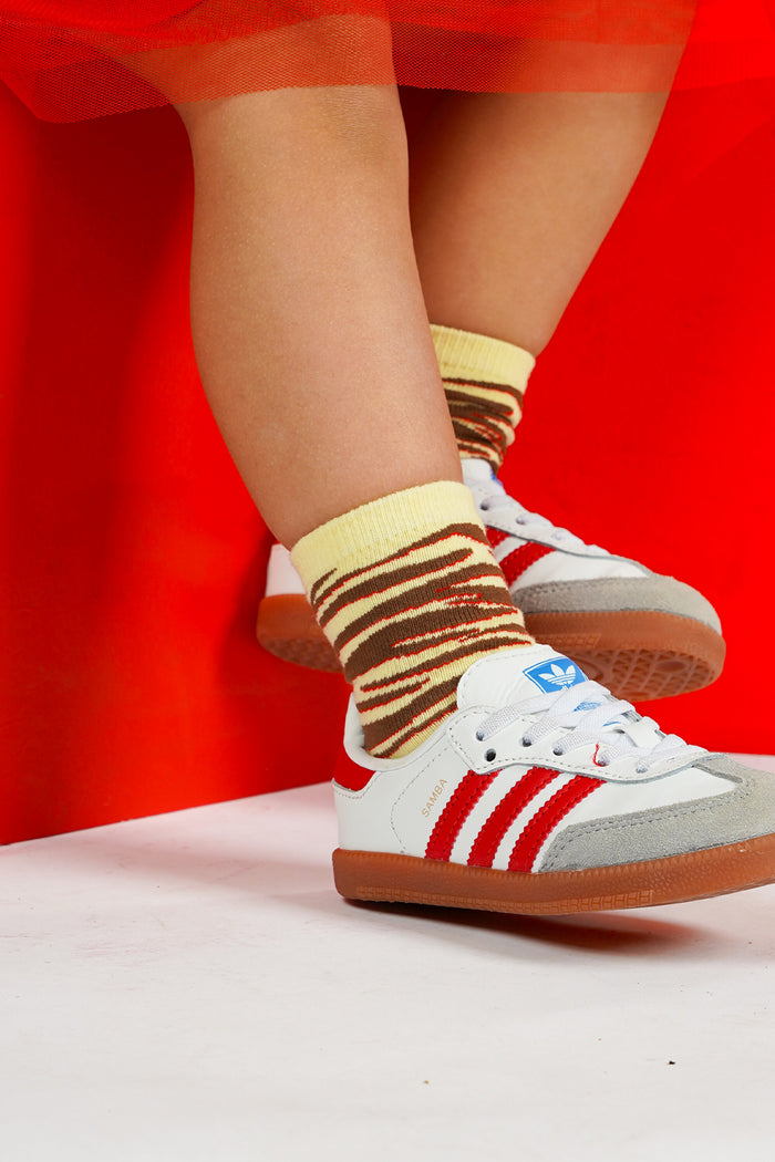 yellow socks with brown and red wavy zebra stripes, posed against a bright red background.