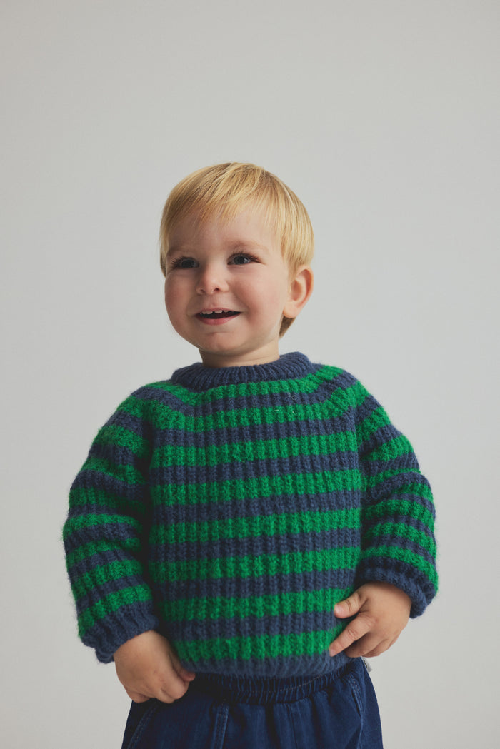 Child wearing a green and blue striped sweater against a plain background