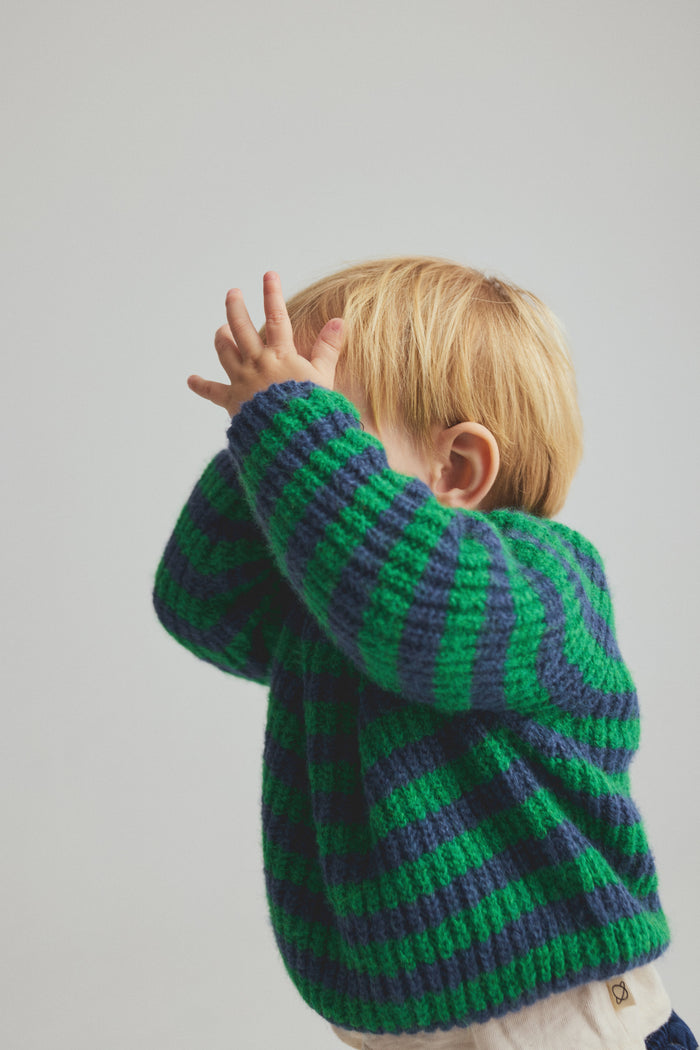 Child wearing a green and blue striped sweater against a plain background